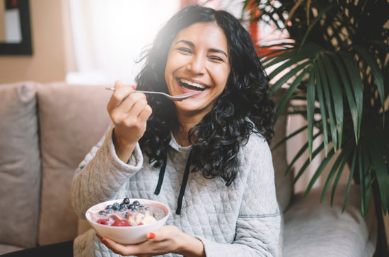 A woman smiling and holding a bowl of yoghurt with fruits