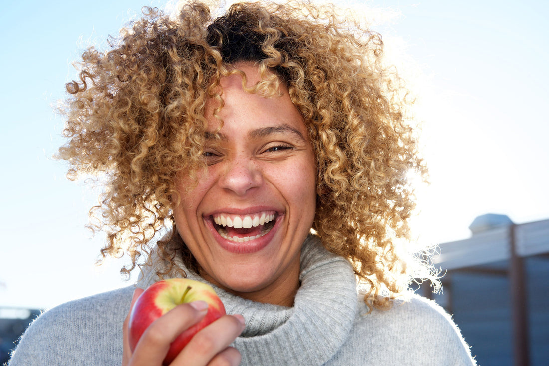 A woman laughing and holding an apple outdoors