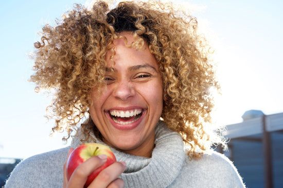 A woman laughing and holding an apple outdoors