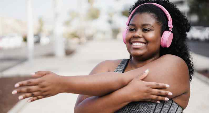 Woman with pink headphones stretching her arms and smiling outdoors