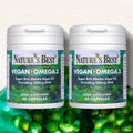 Two bottles of Nature's Best Vegan Omega 3 supplement on a green background with capsules.