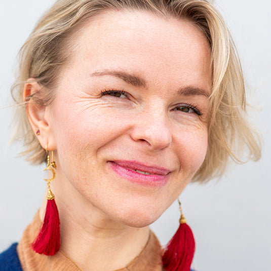 Close-up of a person wearing red tassel earrings against a light background