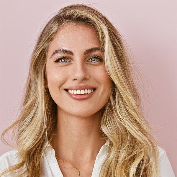 Woman with blonde hair and blue eyes smiling against a pink background