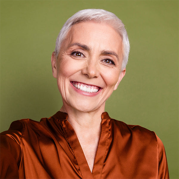 Woman with short white hair wearing a rust-colored shirt against a green background