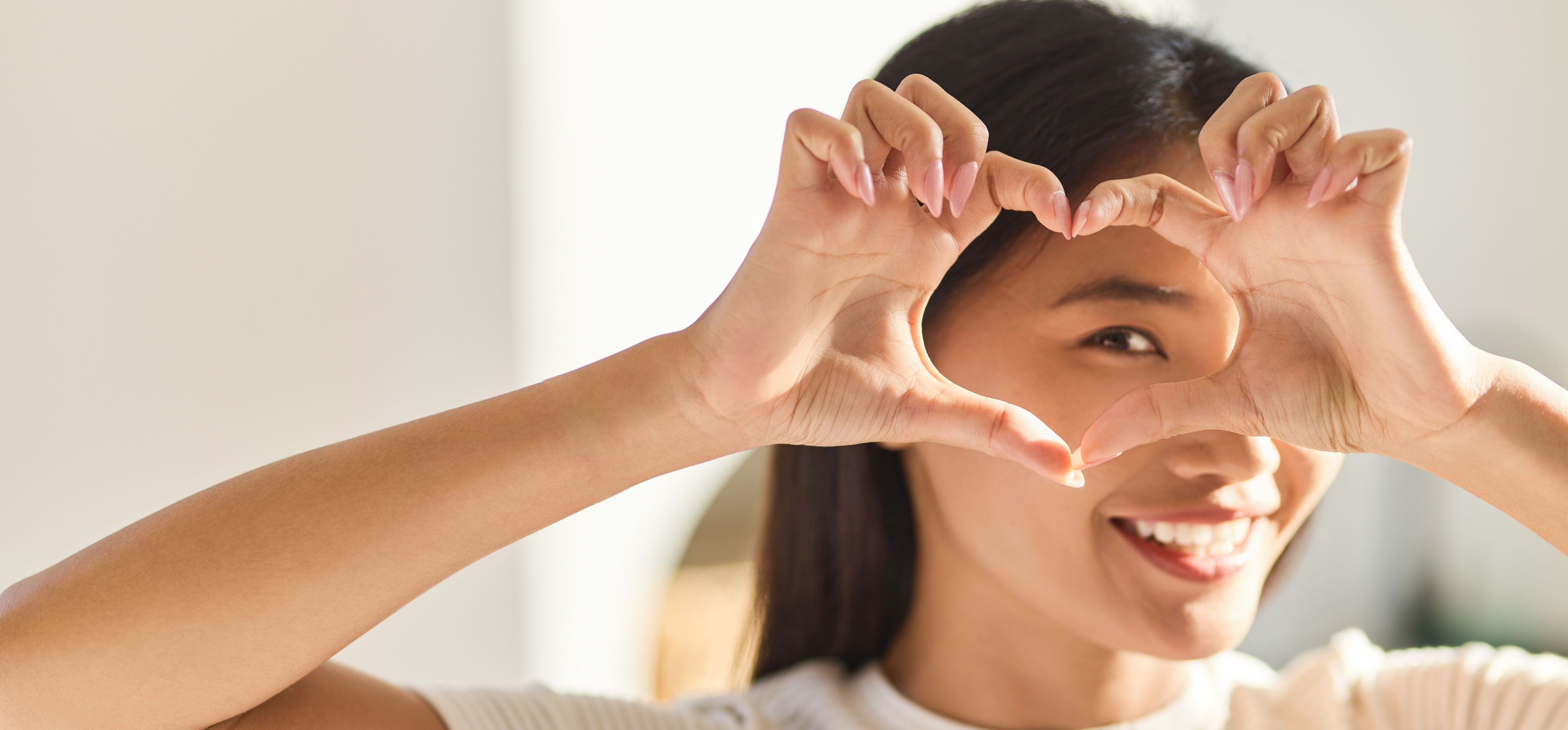 Woman making a heart shape with her hands in front of a blurred background