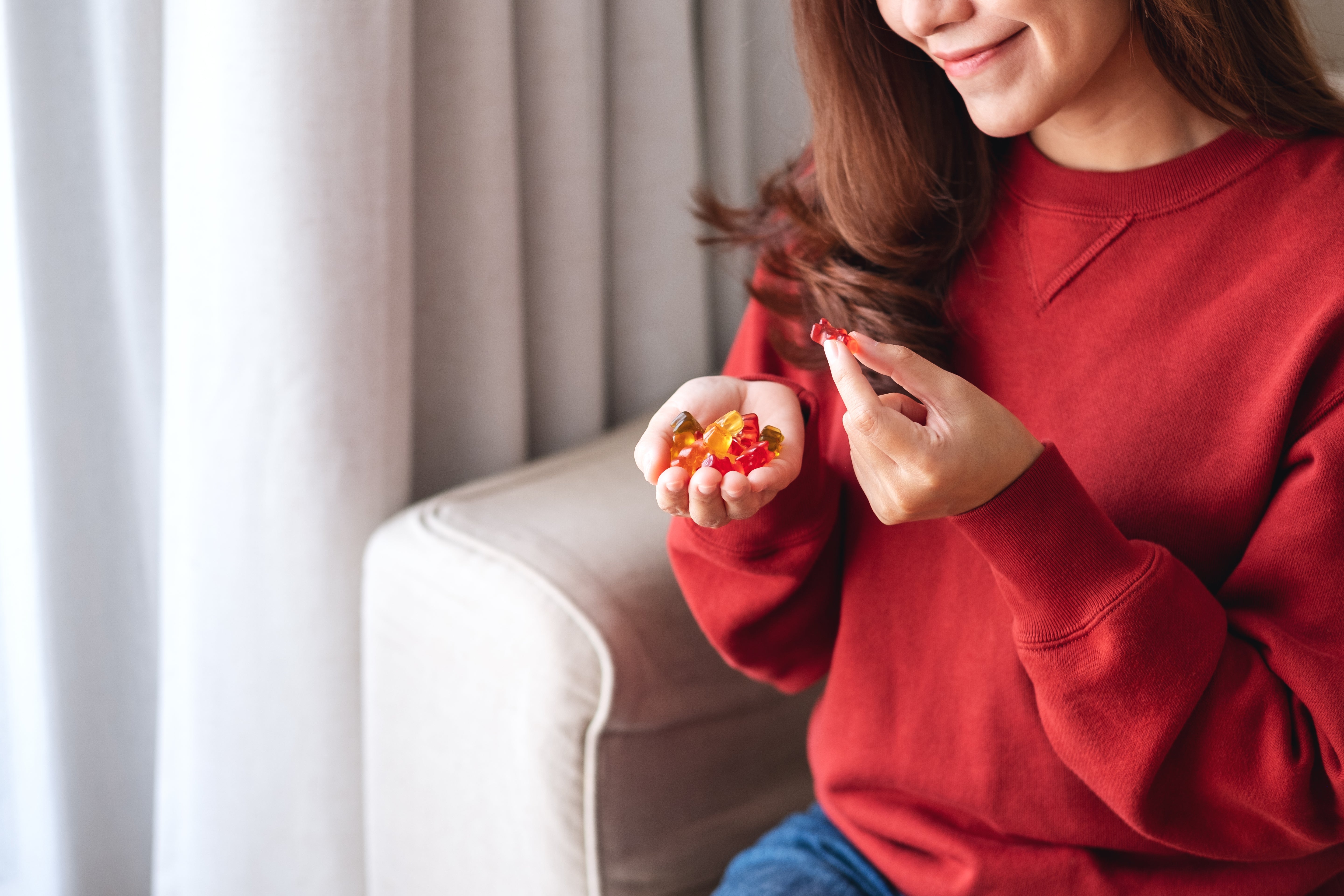Woman in a red sweater holding colorful candies indoors.