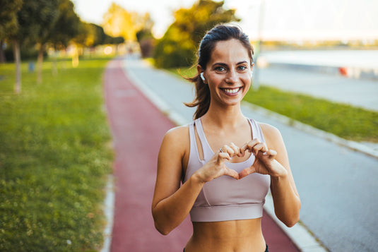 Woman in athletic wear making a heart shape with her hands on a path in a park.