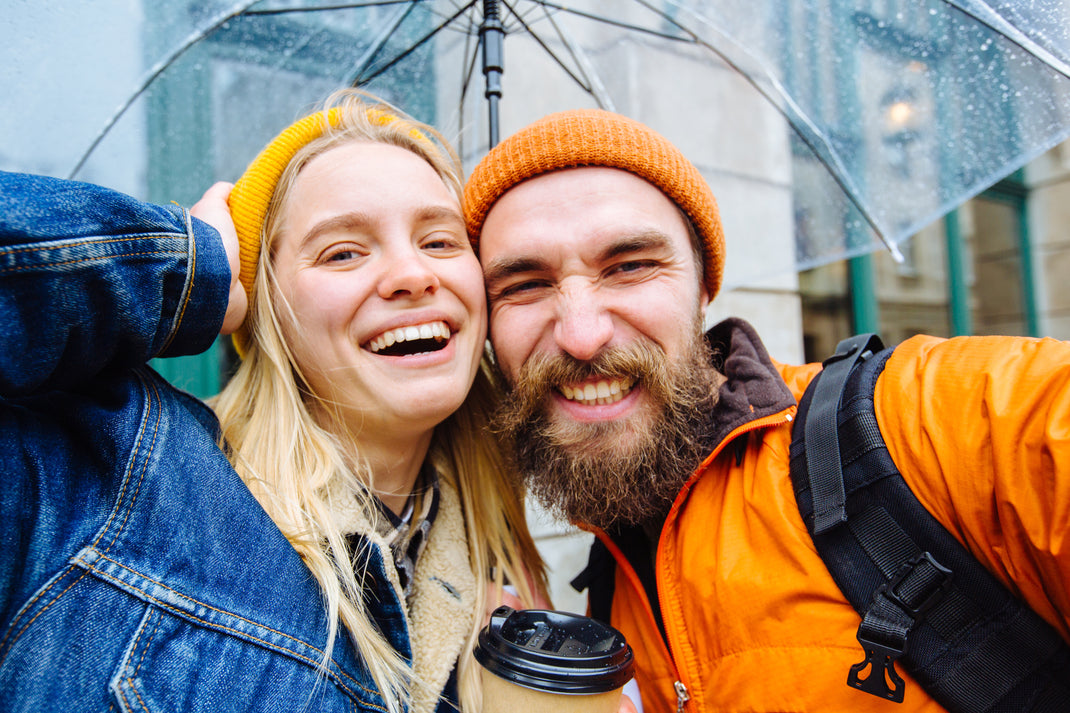 Two people smiling under an umbrella on a rainy day.