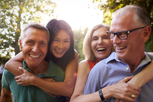 Four people laughing together outdoors with trees in the background