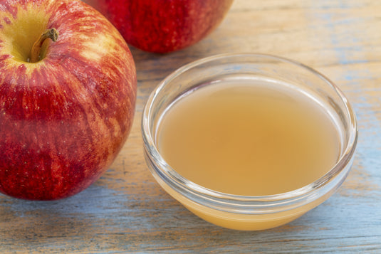 Glass bowl of apple cider vinegar next to red apples on a wooden surface