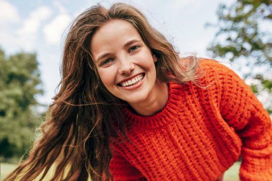 Woman wearing an orange sweater outdoors with trees in the background