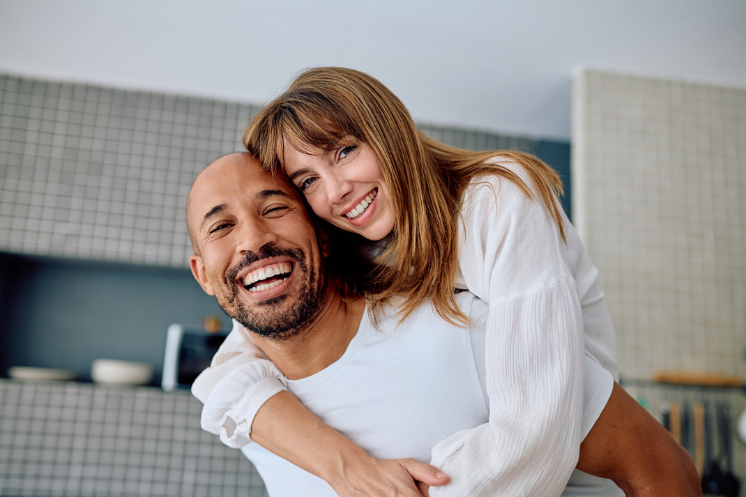 Man and woman hugging in a kitchen, both smiling.