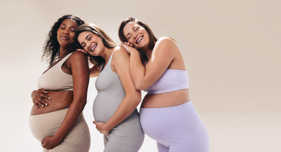 Three pregnant women posing together against a plain background